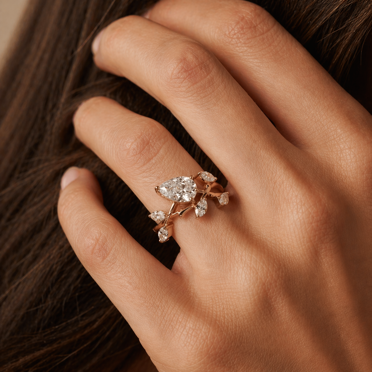 Rose gold pear-shaped diamond engagement ring with vine design, marquise diamond accents, and pear side stones on a hand