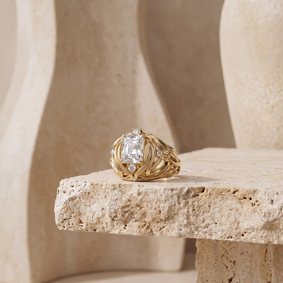 A gold ring with a large rectangular diamond and small accent diamonds, displayed on a textured beige stone pedestal against a softly blurred beige architectural background.