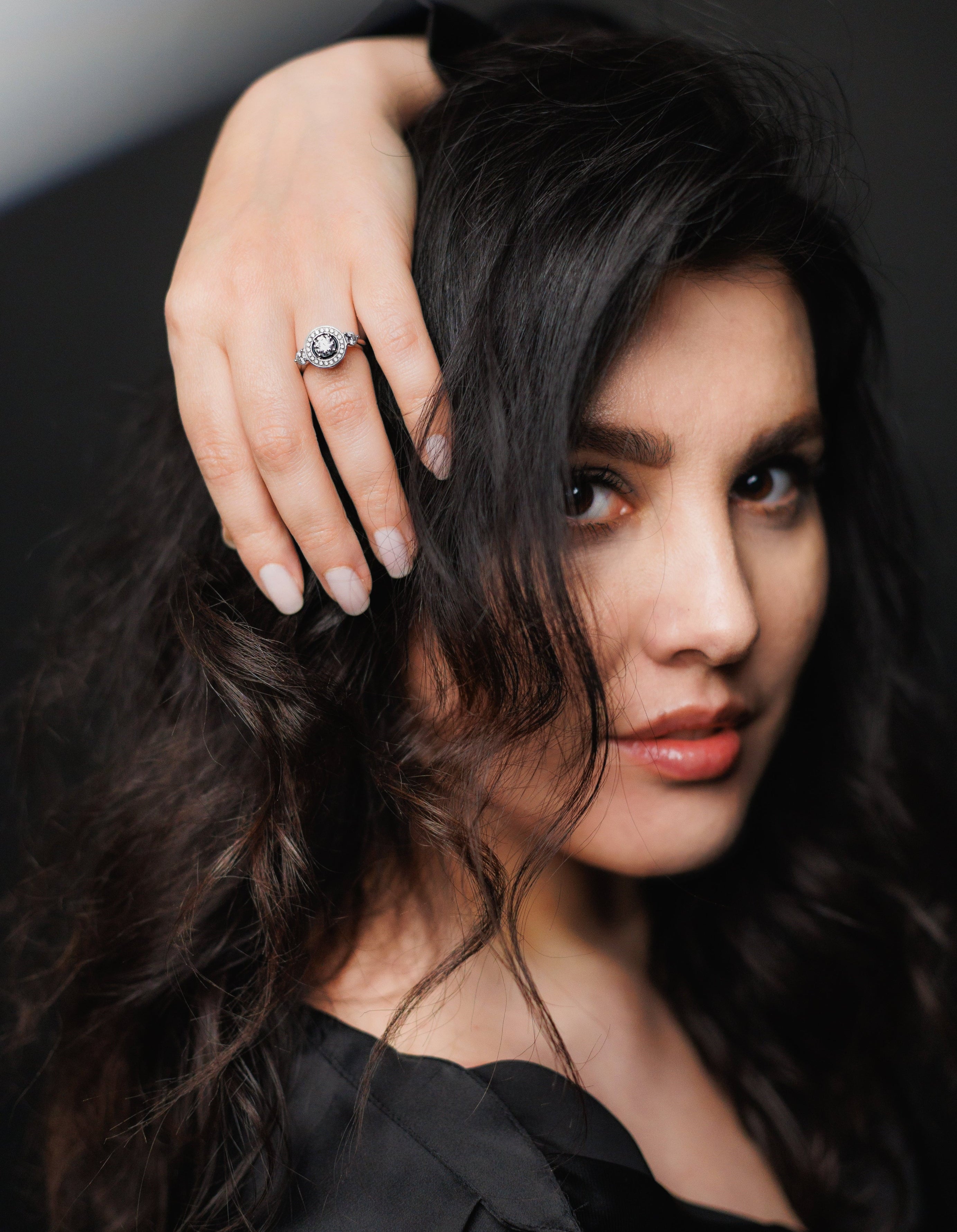Woman with dark hair and a ring on her finger against a dark background