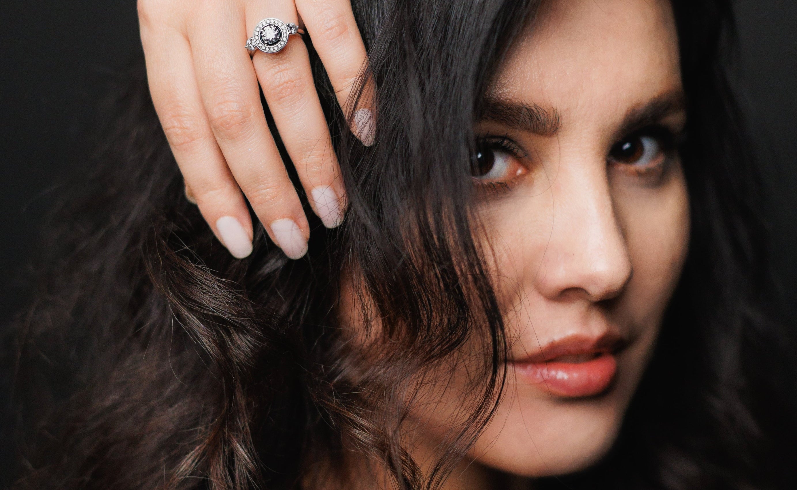 Woman with dark hair and a ring on her finger against a dark background