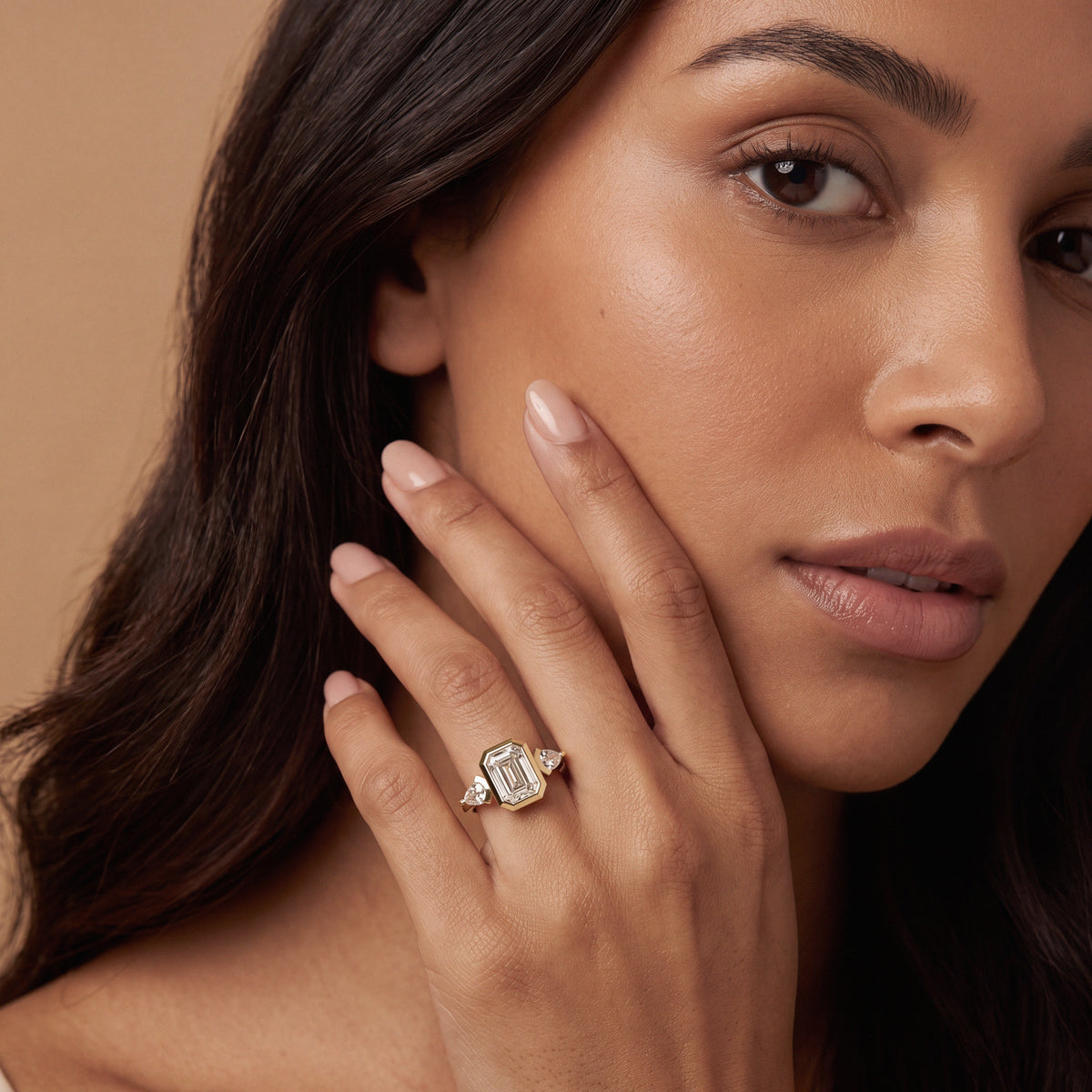 Woman wearing a custom yellow gold three-stone ring with an emerald-cut diamond and pear-shaped side diamonds.