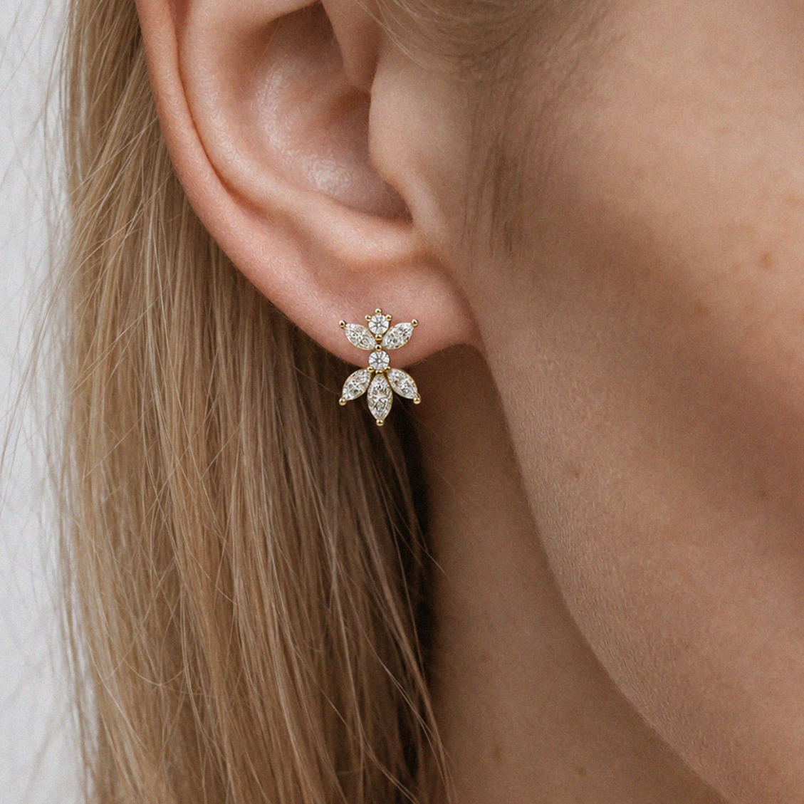 Close-up of an ear wearing a diamond earring with a plain background