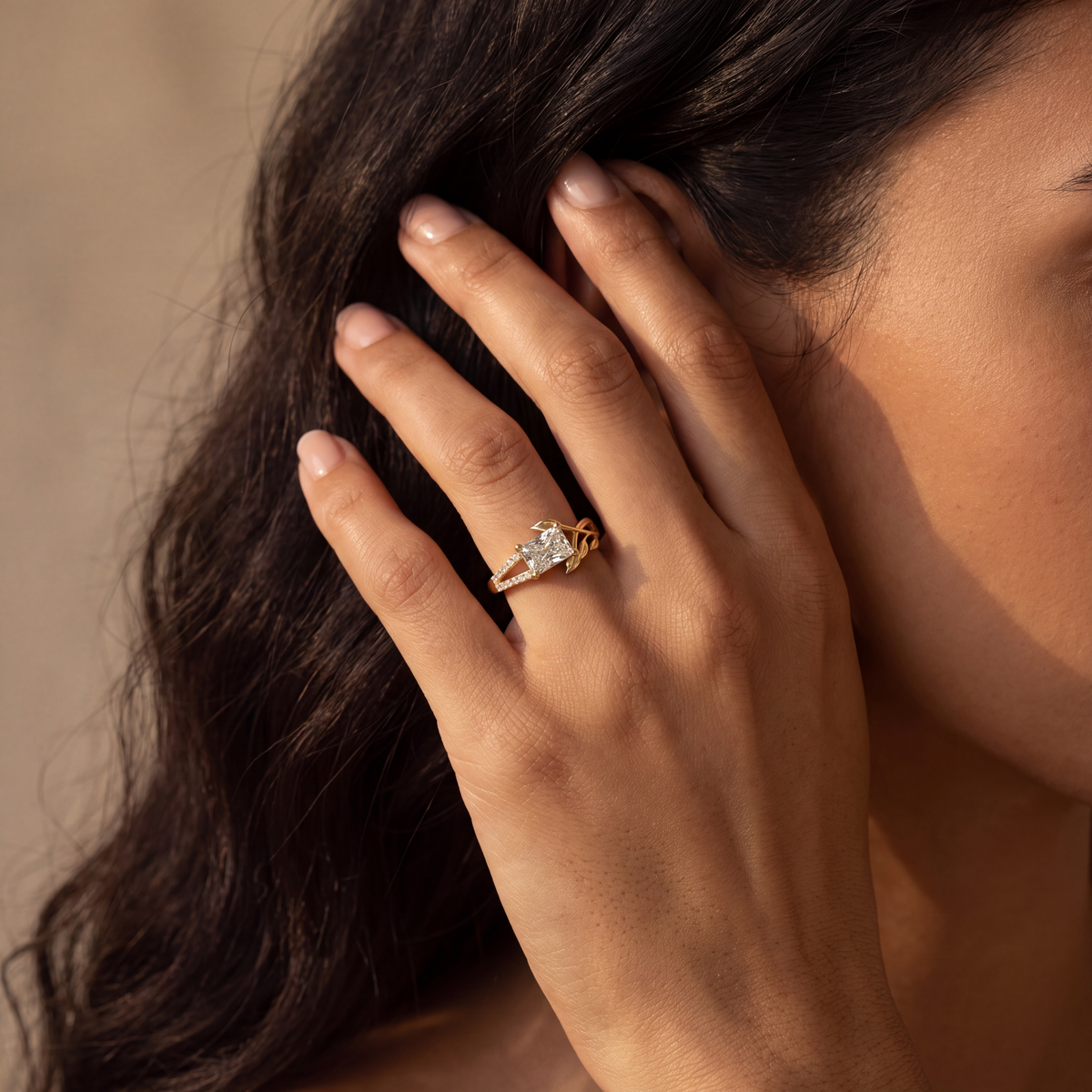 A close-up lifestyle shot of a woman's hand wearing a gold ring with a central clear gemstone, set against a warm, softly blurred background.