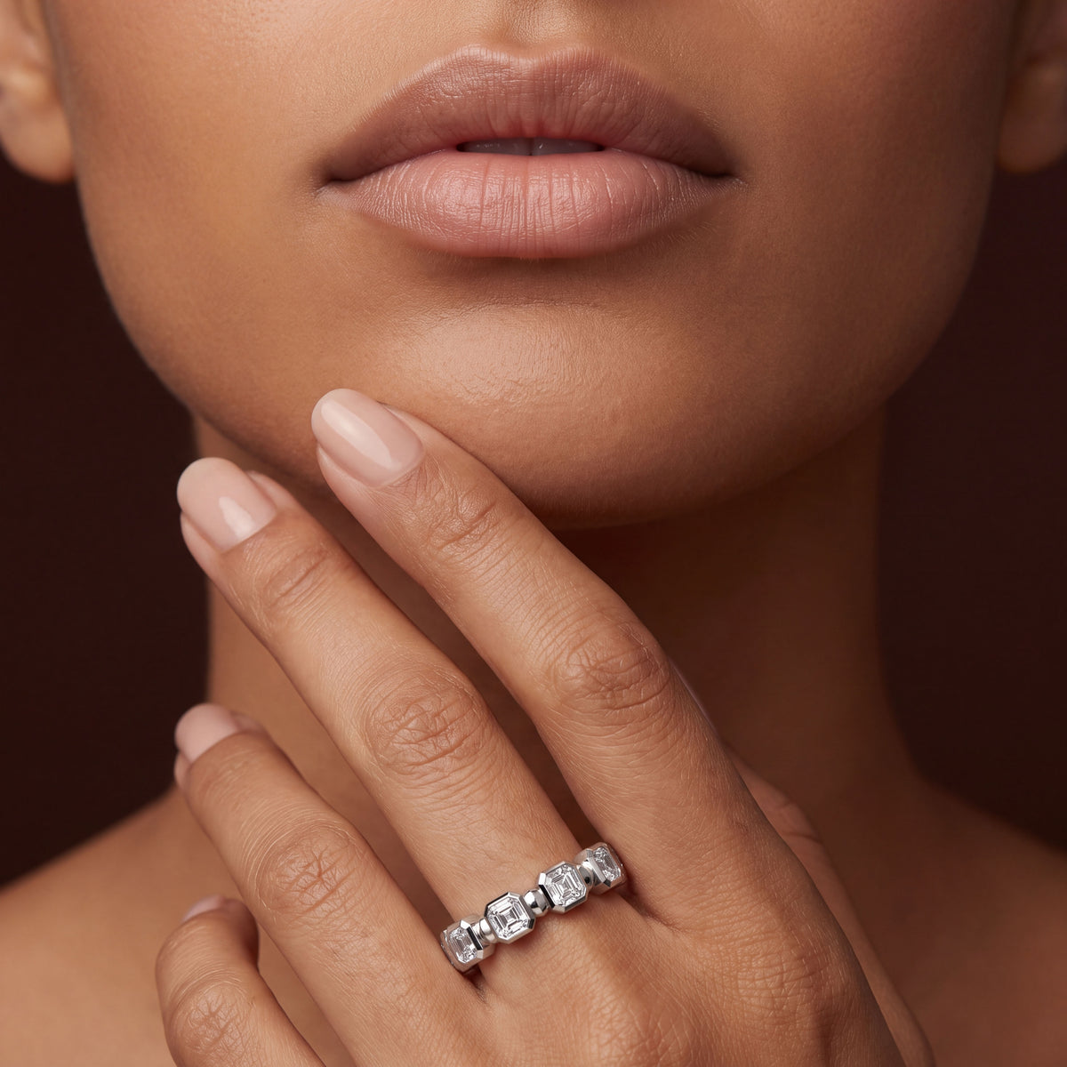 Asscher-cut diamond eternity band with step-cut diamonds in white gold, shown on a woman's hand in a close-up lifestyle image.