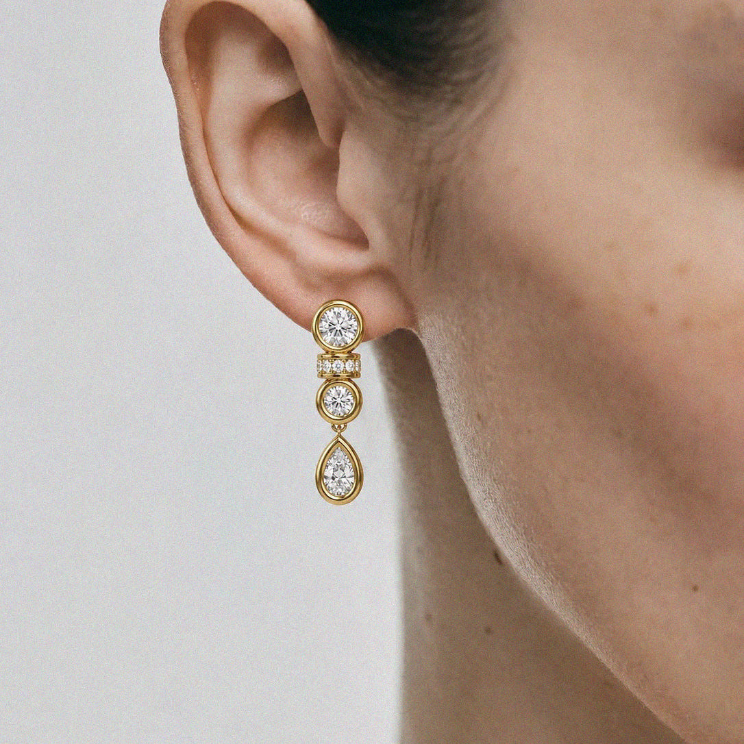 Gold earrings with three dangling stones worn by a person on a light gray background