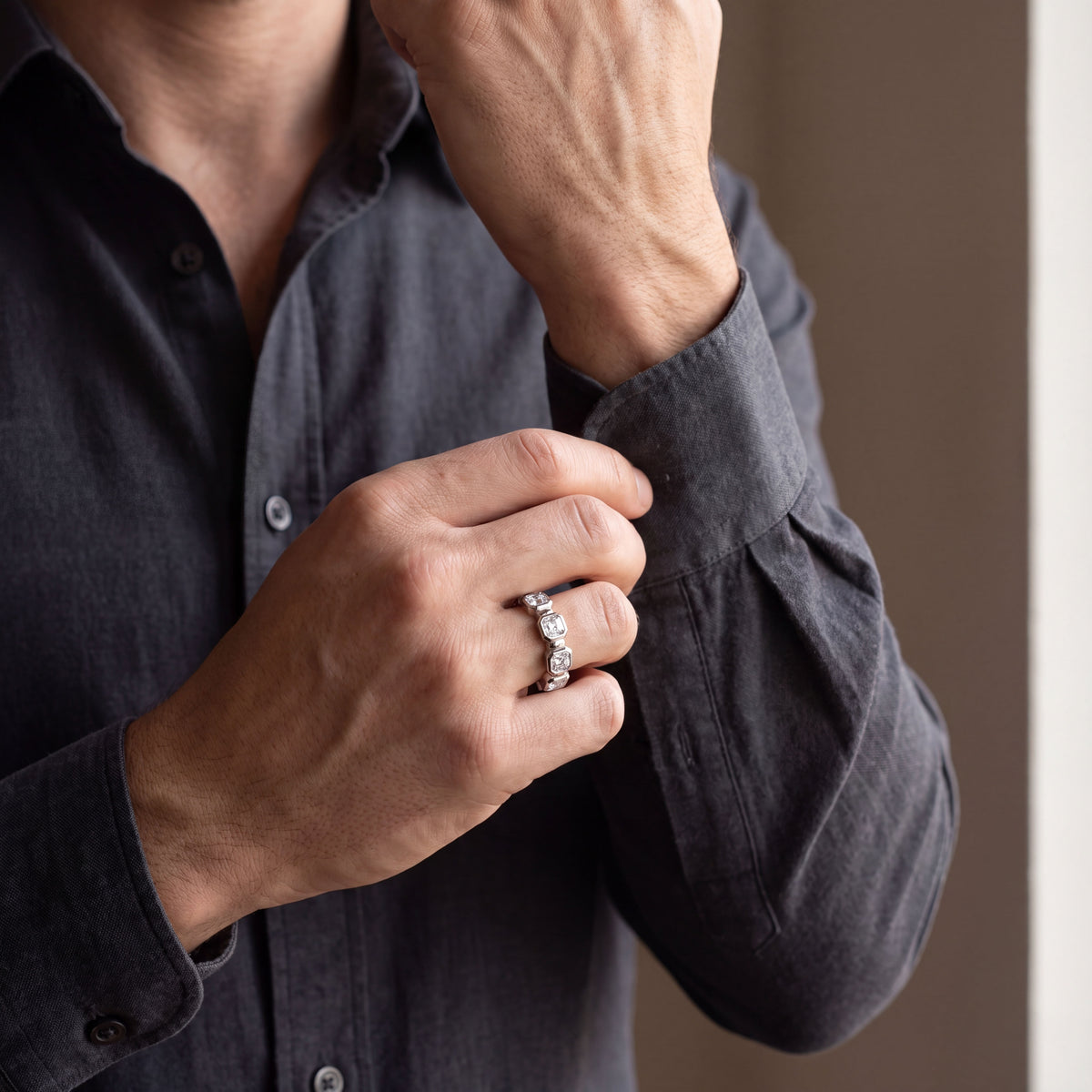 Men’s white gold Asscher-cut diamond eternity band, shown on a man’s hand while adjusting a dark shirt cuff.