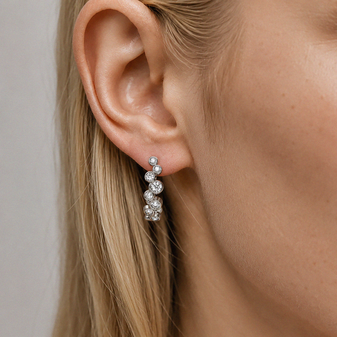 Bubble diamond earrings in white gold with round bezel-set diamonds, shown on the ear.