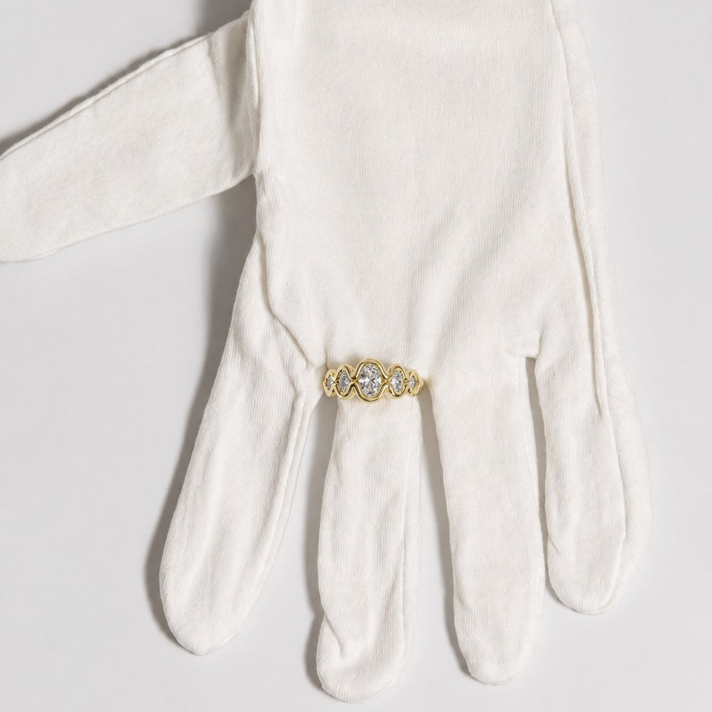 Yellow gold Flow diamond engagement ring with oval and round diamonds, displayed on a white glove.